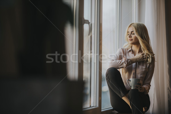 Blonde young woman drinking coffee by window Stock photo © boggy