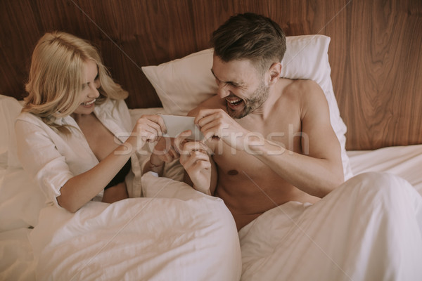 Happy couple in bed and use mobile phone Stock photo © boggy