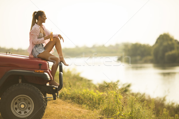 Young woman sits on a car hood and drinks refreshment Stock photo © boggy
