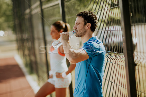 Sporty man drinking water while young woman doing exercise in th Stock photo © boggy