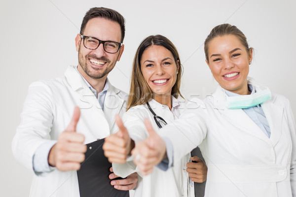 Portrait of three happy doctors who stand smiling and show thumb Stock photo © boggy