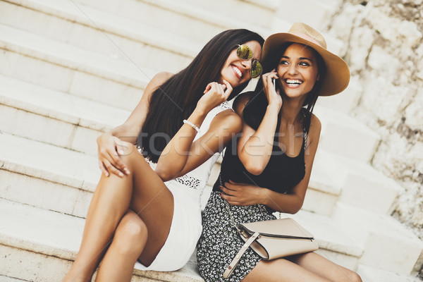 Two women sitting on the stairs outside and using mobile phone Stock photo © boggy