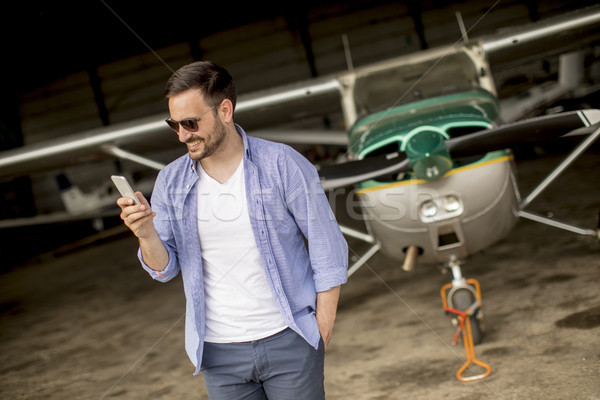 Handsome young pilot checking airplane in the hangar and using m Stock photo © boggy