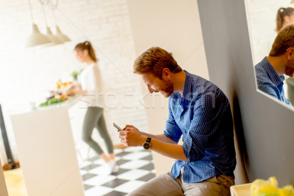 Young man uses a cell phone in the kitchen while  young woman co Stock photo © boggy