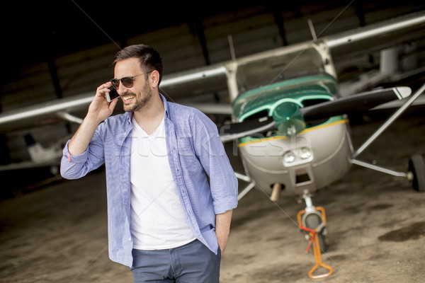 Handsome young pilot checking airplane in the hangar and using m Stock photo © boggy