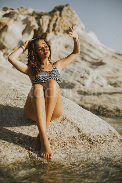 Pretty young woman sitting on the rocky shore by sea Stock photo © boggy