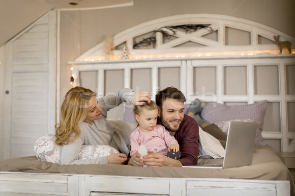 Loving Family Looking At A Laptop Lying Down On Bed In