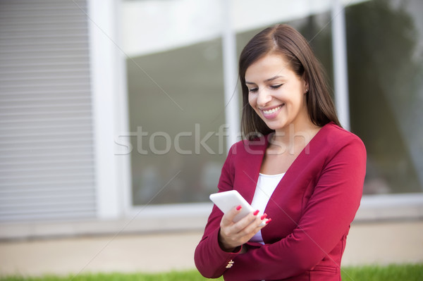 Young businesswoman in red blazer using mobile phone outdoor Stock photo © boggy