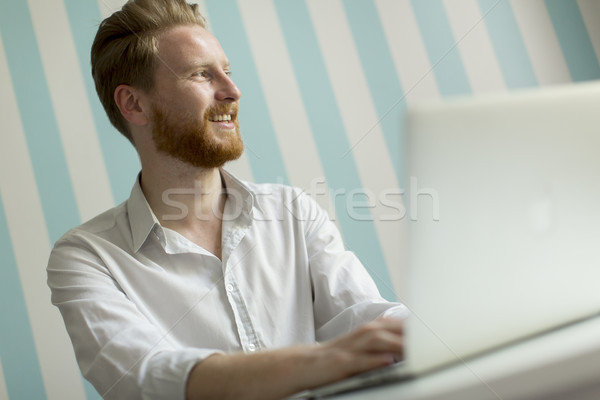 Young redhair man working on laptop in room by the blue striped  Stock photo © boggy