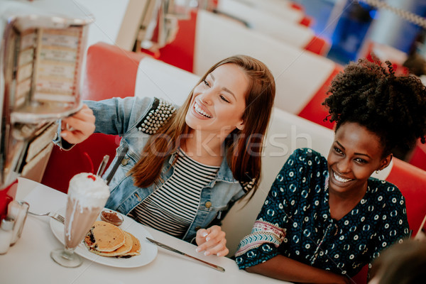 Multiracial female friends eating fast food at a table in the di Stock photo © boggy