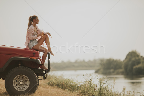 Young woman sits on a car hood and drinks refreshment Stock photo © boggy