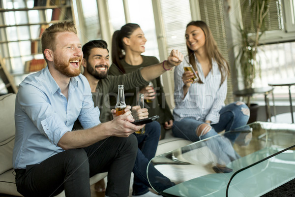 Group of young friends looking at the TV, drinking cider and hav Stock photo © boggy