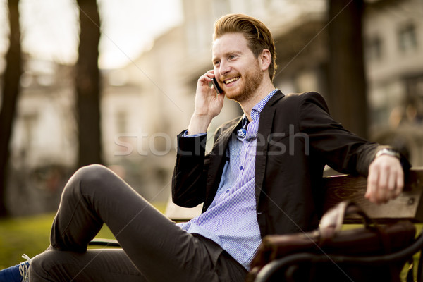 Young redhair businessman with mobile phone on a bench Stock photo © boggy