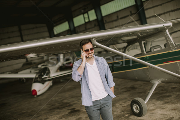 Stock photo: Handsome young pilot checking airplane in the hangar and using m