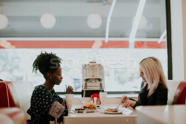 Multiracial female friends eating fast food at a table in the di Stock photo © boggy