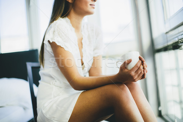 Young woman drinking coffee and dreaming on a chair by the windo Stock photo © boggy