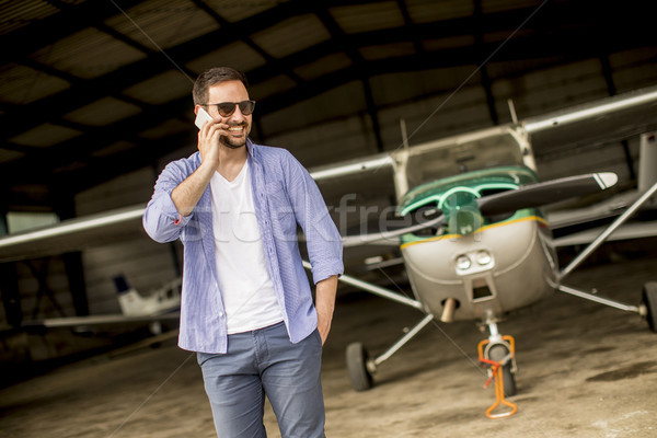 Handsome young pilot checking airplane in the hangar and using m Stock photo © boggy