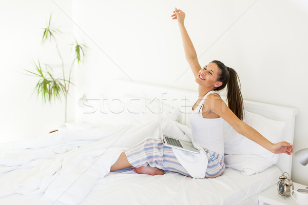 Young woman stretching in bed while her lap top standing on legs Stock photo © boggy