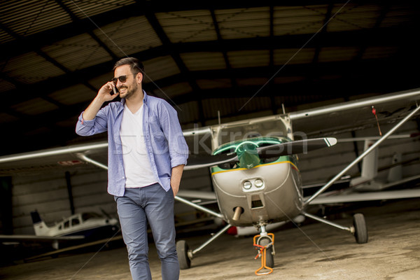 Handsome young pilot checking airplane in the hangar and using m Stock photo © boggy