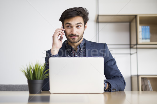 Young businessman working on laptop and talking on the mobile ph Stock photo © boggy