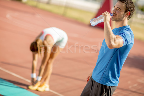 Sporty man drinking water while young woman doing exercise in th Stock photo © boggy