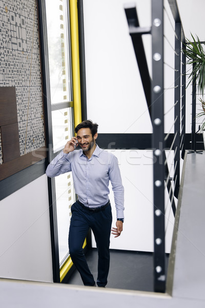 Young businessman talking on mobile phone and climbing on the st Stock photo © boggy