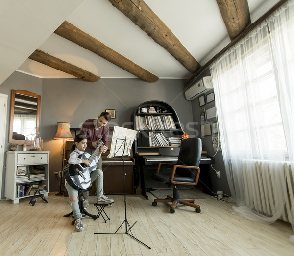 Stock photo: Cute little girl with guitar teacher in the room