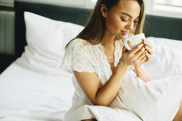 Young woman sitting on a bed and drinking coffee after waking up Stock photo © boggy