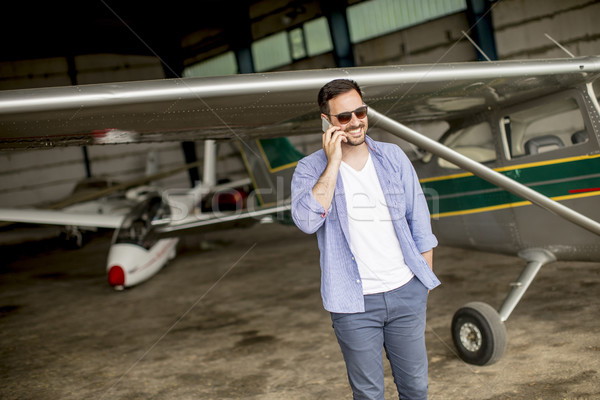 Stock photo: Handsome young pilot checking airplane in the hangar and using m