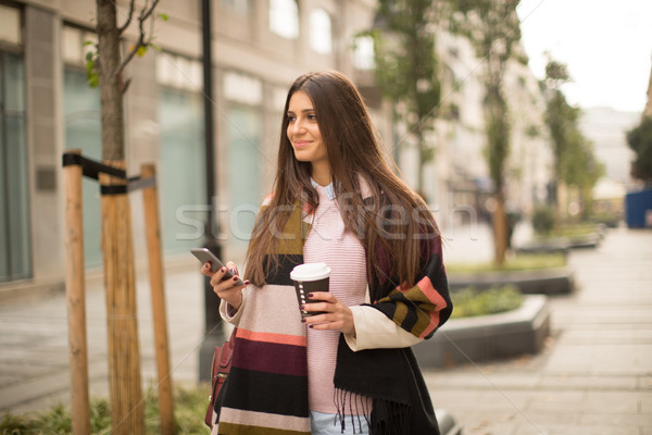 Stock photo: Woman standing outside, drinking coffee to go and holding a mobi