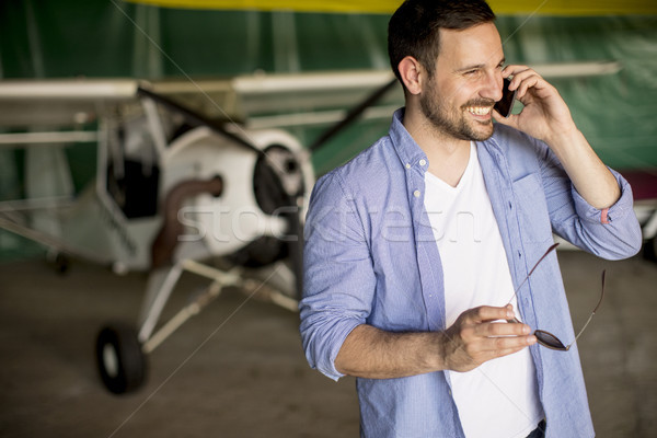 Handsome young pilot checking airplane in the hangar and using m Stock photo © boggy