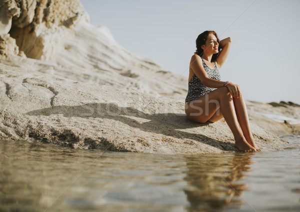 Pretty young woman sitting on the rocky shore by sea Stock photo © boggy