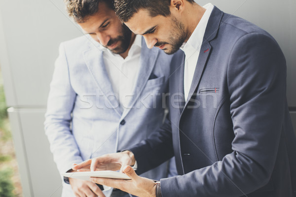 Two young businessmen looking at tablet in front of a black wall Stock photo © boggy