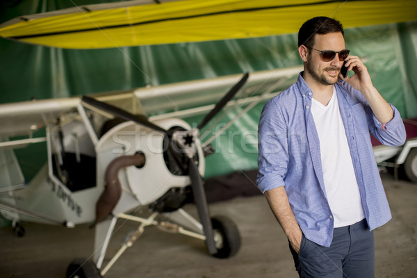 Handsome young pilot checking airplane in the hangar and using m Stock photo © boggy