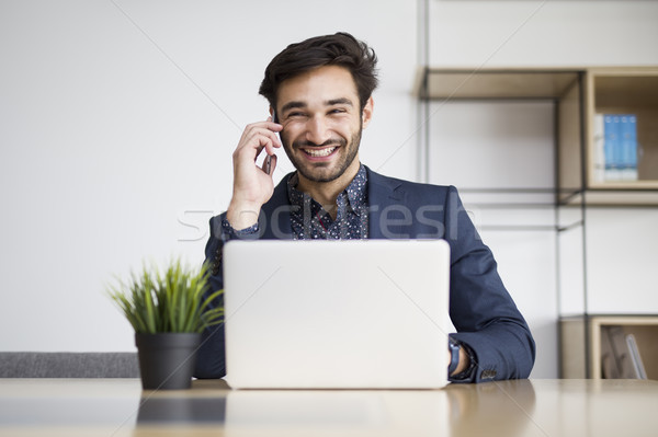 Young businessman working on laptop and talking on the mobile ph Stock photo © boggy
