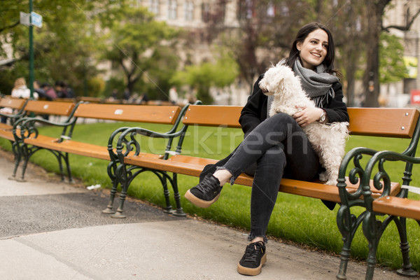 Stock photo: Young woman sitting in the park and holding a small dog in her l