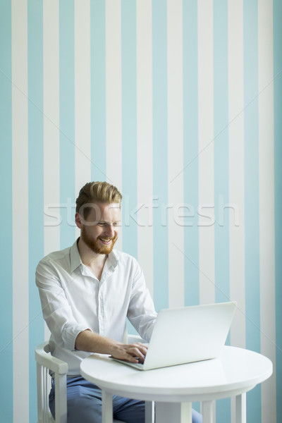 Young redhair man working on laptop in room Stock photo © boggy
