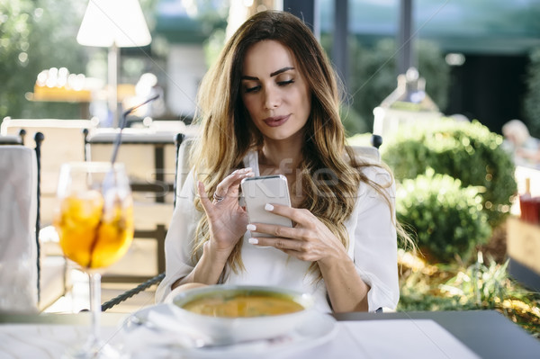 Attractive young woman sitting in restaurant and using mobile ph Stock photo © boggy