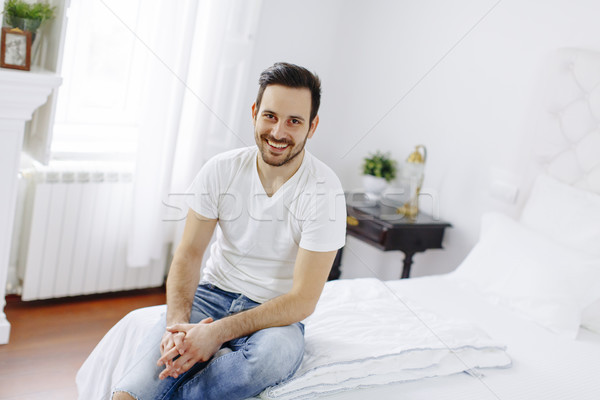 Smiling young man sitting on the bed in the bedroom Stock photo © boggy