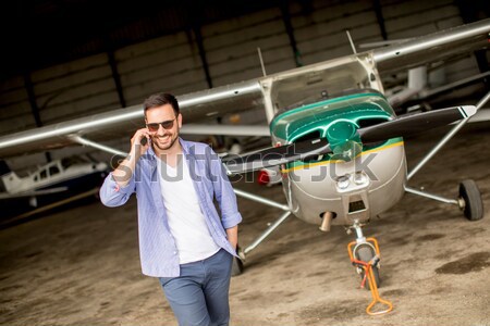 Handsome young pilot checking airplane in the hangar and using m Stock photo © boggy