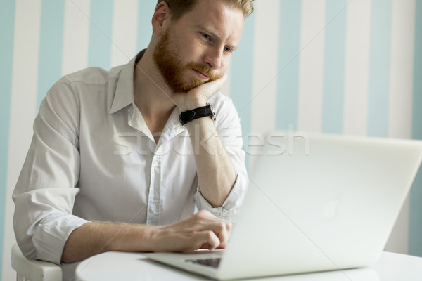 Young redhair man working on laptop in room by the blue striped  Stock photo © boggy