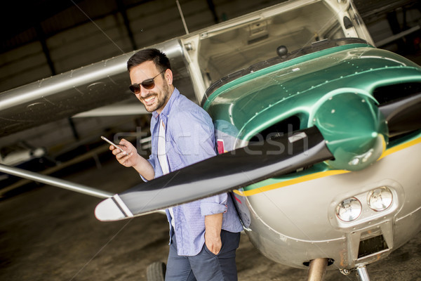 Handsome young pilot checking airplane in the hangar and using m Stock photo © boggy