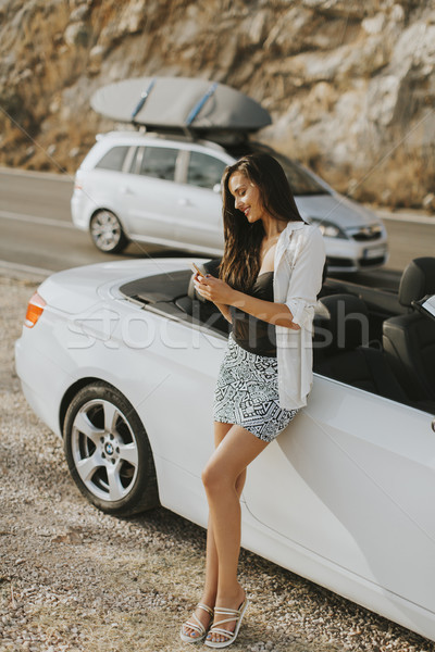 Woman uses a mobile phone and stands next to cabriolet in the su Stock photo © boggy