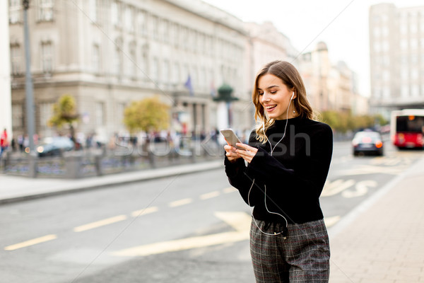 Young brunette woman using mobile while standing on street and   Stock photo © boggy