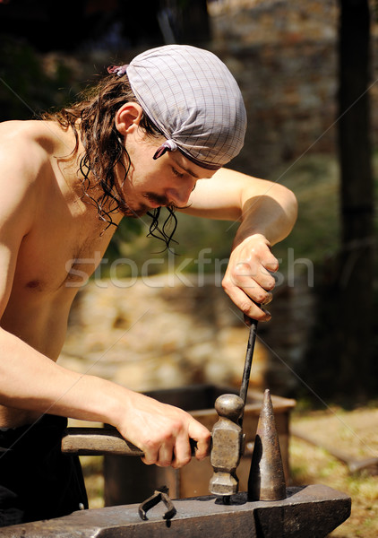 Stock photo: Young blacksmith hammering hot iron on anvil