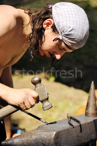 Young blacksmith hammering hot iron on anvil Stock photo © brozova