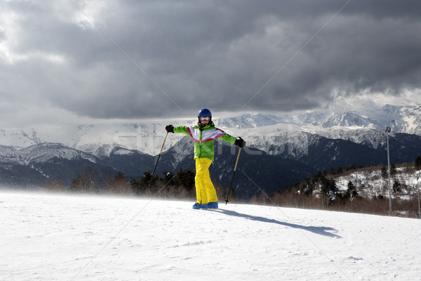 Stock photo: Happy young skier with ski poles in sun mountains and cloudy gra