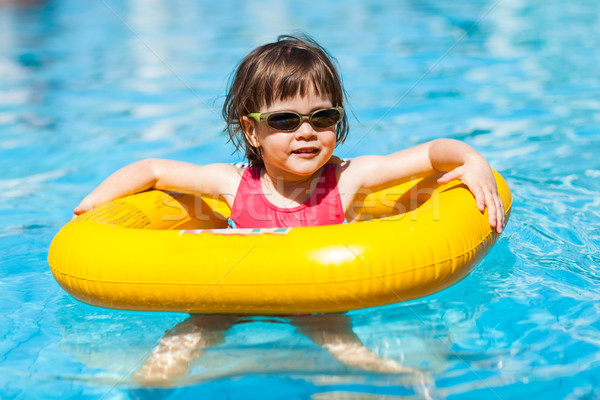 Stock photo: Cute girl swims in a pool in a yellow life preserver 