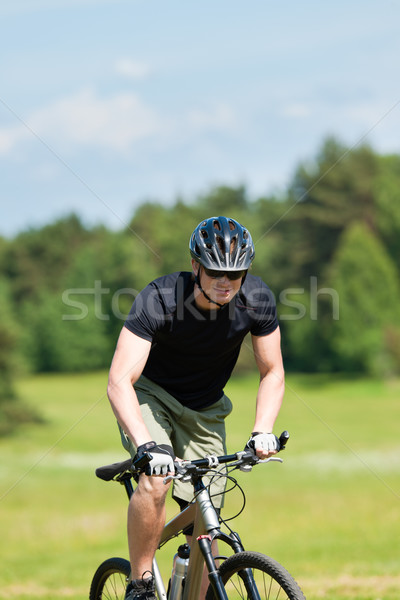 Stock photo: Sportive man mountain biking uphill sunny meadows
