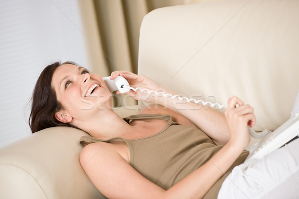 Stock photo: On the phone home: Smiling woman lying down on sofa calling